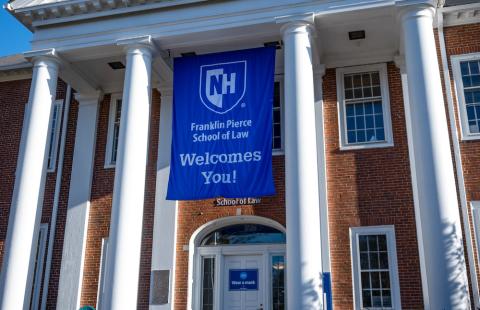 Vertical picture of front steps of law school with blue UNH FP Welcomes You flag hanging down