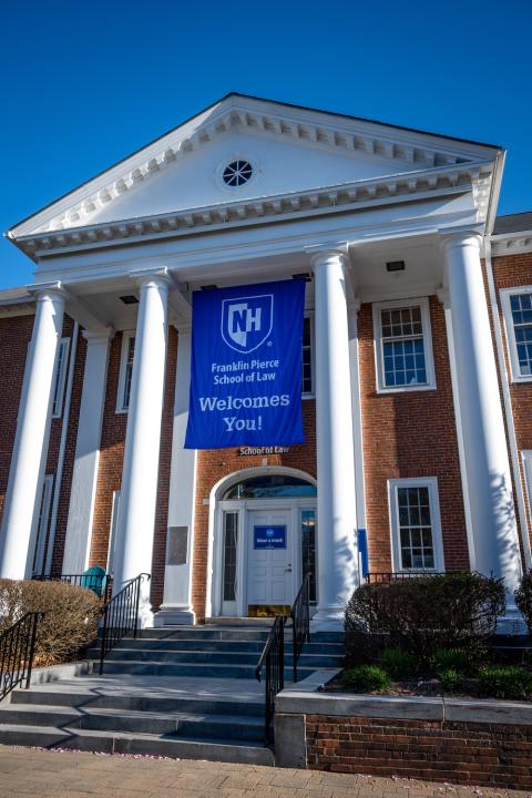 Vertical picture of front steps of law school with blue UNH FP Welcomes You flag hanging down